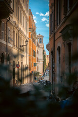 Obraz premium Narrow European street with historic buildings and pedestrians under a bright blue sky. Rome Italy