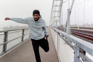 Obraz premium Focused Black male athlete balancing during outdoor workout on a foggy bridge. Dynamic movement, urban fitness training, strength, coordination and determination in a modern city setting