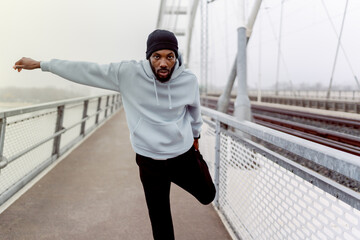 Focused Black male athlete balancing during outdoor workout on a foggy bridge. Dynamic movement, urban fitness training, strength, coordination and determination in a modern city setting