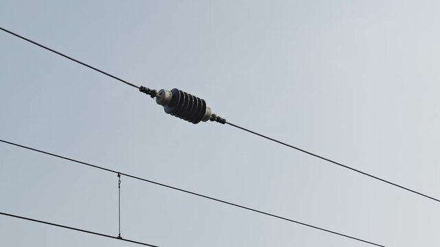 Closeup of ceramic insulator mounted on overhead railway electric wire, isolating high voltage traction line against clear sky, showing power infrastructure detail