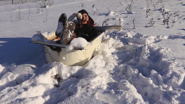 Creative winter lifestyle shot: a woman lies in an open-air bathtub amidst the snow, holding a glass of snow in the form of a cocktail