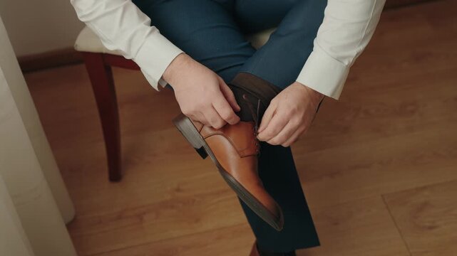 Close view of hands fastening leather boot while seated indoors