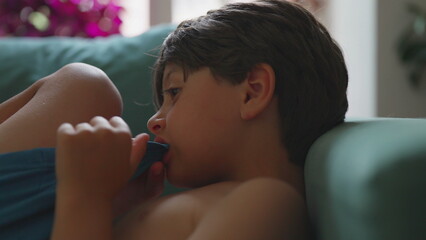 Close-up of boy biting fabric while curled on couch, introspective mood and ambient lighting...