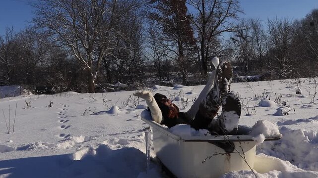 Young woman in old bathtub in the middle of a snowy field enjoying the winter sun, humorous atmosphere, freedom, relaxation and creative winter mood.