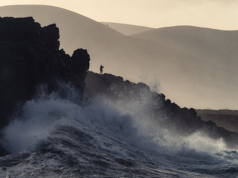 Silhouette on Rocky Cliff Above Powerful Crashing Waves at Dramatic Coastline