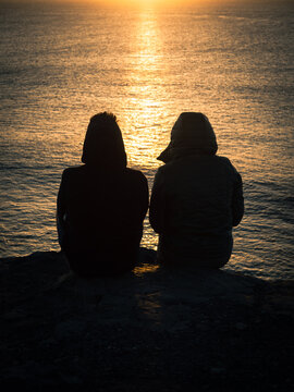 Silhouetted Couple Sitting by the Water at Sunset