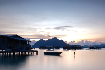Wooden boat floating near stilt houses at sunrise