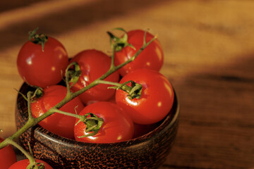 Fresh cherry tomatoes in rustic wooden bowl on wooden table, bathed in warm sunlight, creating vibrant and inviting atmosphere