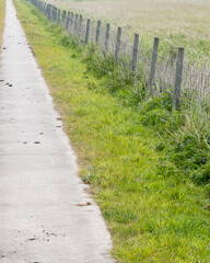 Pathway along a grassy area with a fence in a rural setting during the day