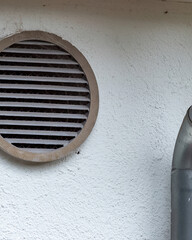 Ventilation opening on a building wall near a metal pipe during daylight hours