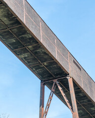 View of a long elevated walkway with metal supports against a clear sky at midday