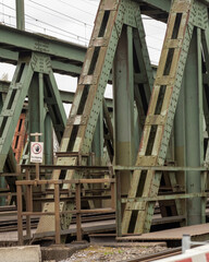 Old railroad bridge structure with green metal supports in an urban area during a cloudy day