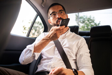 Business man recording voice message on smartphone in back seat during commute