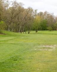 Golf course view with trees and grass on a cloudy day in the early afternoon during spring season