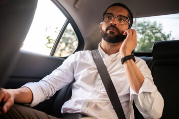 Business man using smartphone in back seat during urban commute
