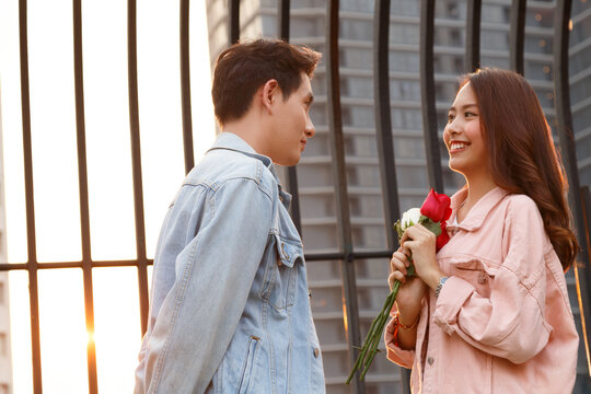 young happy couple love and romantic at first date relationship. asian teenage woman surprise and smiling at boyfriend gives red rose flowers at dinner in valentine day. couple and happiness concept.