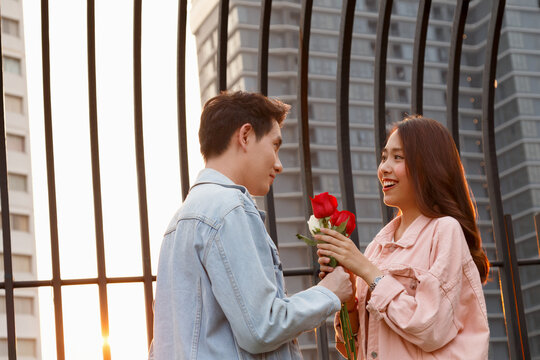 young happy couple love and romantic at first date relationship. asian teenage woman surprise and smiling at boyfriend gives red rose flowers at dinner in valentine day. couple and happiness concept.