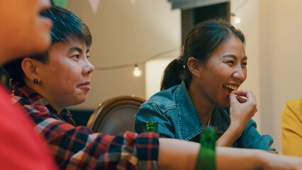 Group of multiethnic adult Asia friend drink alcohol beer bottle glass and fun talk laugh enjoy hangout party at dining table in night life indoor home. Happy hour millennial generation inside house.