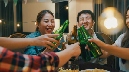 Group of multiethnic young adult Asia friend drinking alcohol beer bottle glass and having fun laugh enjoy hangout party in night life indoor home. Happy hour time millennial generation inside house.