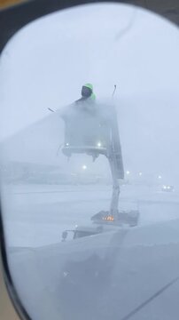 Deicing operation airport worker using elevated platform spraying aircraft wing with deicing fluid during snowy winter conditions, 4k footage