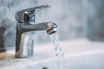 Water flows from a modern faucet into a sink in a bathroom, showing daily use of plumbing fixtures in a clean environment