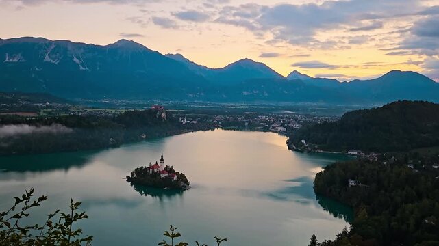 Sunrise light over Lake Bled with calm water and surrounding mountains at dawn, establishing pan right over valley