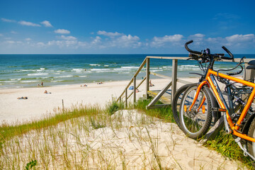 Fototapeta premium Scenic view of Curonian Spit beach with orange bicycles parked on grassy dunes near wooden stairs overlooking Baltic Sea coastline in summer