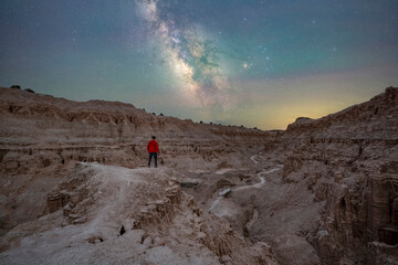 Night hiker in a red jacket standing near a rocky ledge overlooking Cathedral Gorge State Park Nevada