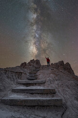 Rocky steps leading towards a night hiker pointing towards the Milky Way Galaxy in Nevada 
