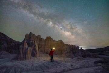 Man hiking in the desert at a unique rock formation under the milky way galaxy in Nevada