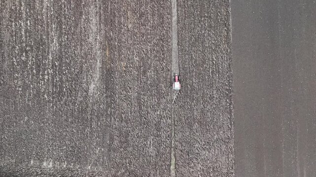 Aerial overhead view of small tractor moving across wide plowed farmland showing agricultural scale