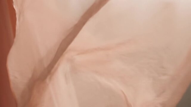 Close-up of a flowing peach-colored fabric with soft folds and creases