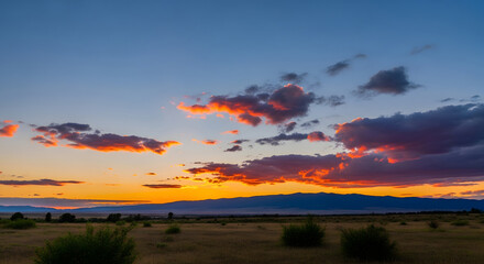 A vibrant sunset over a grassy plain with distant mountains and colorful clouds