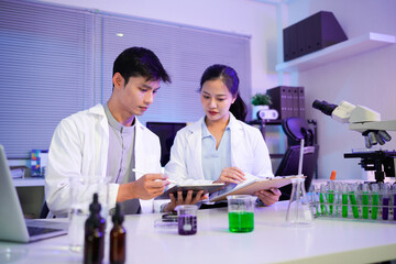 Asian Scientists Collaborating in Modern Lab, Two young asian scientists, a man and a woman work together in a modern laboratory setting, using a tablet and clipboard to analyze data