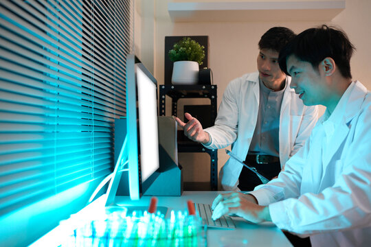 Two scientists are working together in a lab at night, They are looking at a computer screen, computer mock up white screen