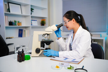 Fototapeta premium A female scientist using a microscope for research in a modern lab. She is focused and dressed in a lab coat, gloves, and safety glasses