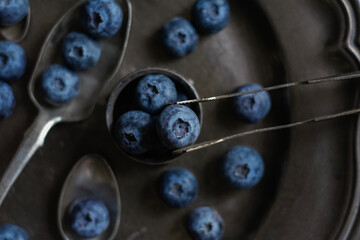 Moody dark-tone close-up of fresh blueberries arranged in a small vintage metal bowl and scattered...