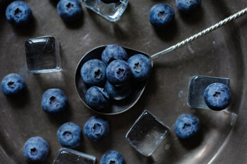 Moody dark-tone close-up of fresh blueberries arranged in a small vintage metal bowl and scattered...