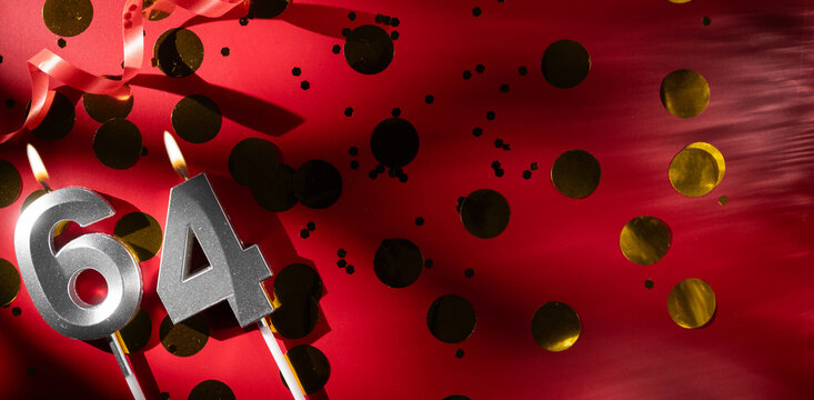 Concept of celebrating birthday and anniversary. Number 64 sixty-four silver celebration birthday candle on festive red background with large golden confetti. Sixty-four years birthday.