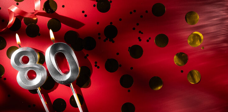 Concept of celebrating birthday and anniversary. Number 80 eighty silver celebration birthday candle on festive red background with large golden confetti. Eighty years birthday. - Powered by Adobe