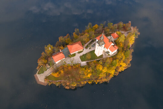 Aerial view of the tranquil island in a still lake, topped with a church and surrounded by trees ablaze with autumn colors, Spodnja Lua, kofja Loka, Slovenia.