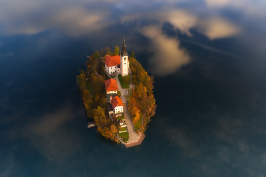 Aerial view of the island church rising majestically from the still waters, framed by autumn foliage and a soft mist, Spodnja Lua, kofja Loka, Slovenia.