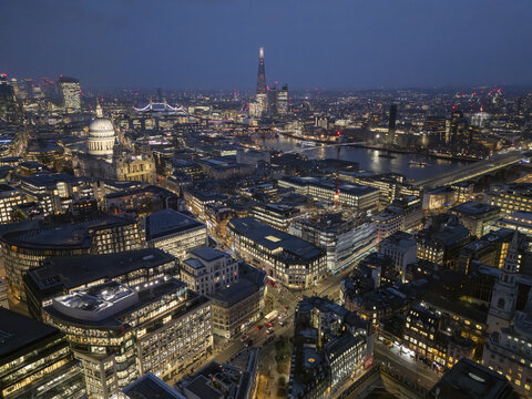 Aerial view of the city lit up with warm lights contrasting against the cool tones of the night sky, St. Paul's Cathedral and the River Thames visible, London, United Kingdom.