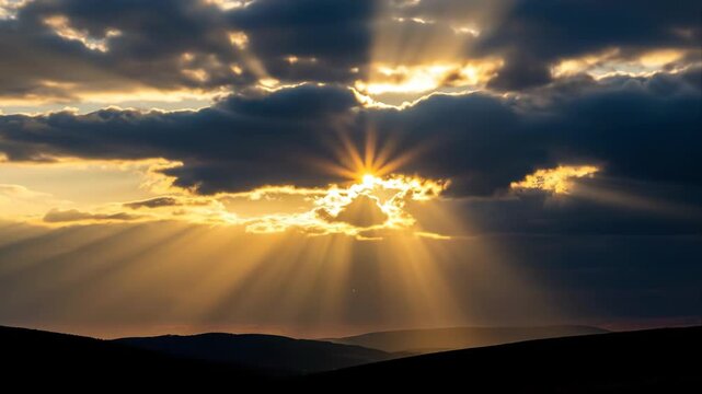 Sunbeams break through dark clouds over rolling hills at sunset.