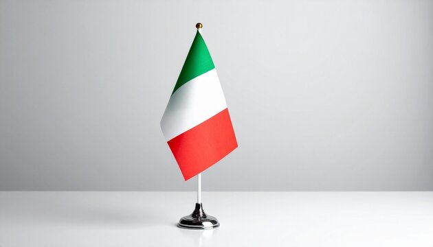Italian table flag with vertical green, white, and red stripes mounted on silver stand, placed on white surface with light gray background.