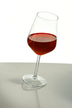 Minimal still life of a tilted wine glass with red beverage on a reflective surface, isolated on white background. Conceptual composition suggesting balance, elegance, and modern design.