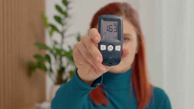 A woman checks her blood sugar level at home using a glucometer. The reading shows a high level of 163 mg dL. Managing diabetes is important for health.