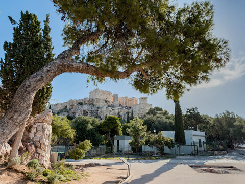 Acropolis of Athens and propylaea gate, visitors on the ruins, green trees, blue sky, view from Areopagus hill, Greece.