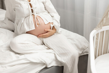 Pregnant woman in a bright nursery holding baby clothes near a crib. Soft natural light, cozy home interior, motherhood anticipation, maternity lifestyle, family love, neutral tones, calm atmosphere.