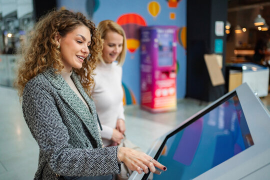 Women friends using interactive digital kiosk touch screen